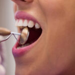 Close-up of dentist examining a female patient with tools at dental clinic